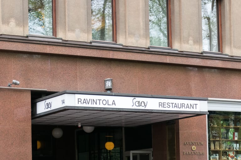 Entrén till restaurang Savoy i Helsingfors, med en vit markis med texten Ravintola Savoy Restaurant under en rödbrun stenfasad