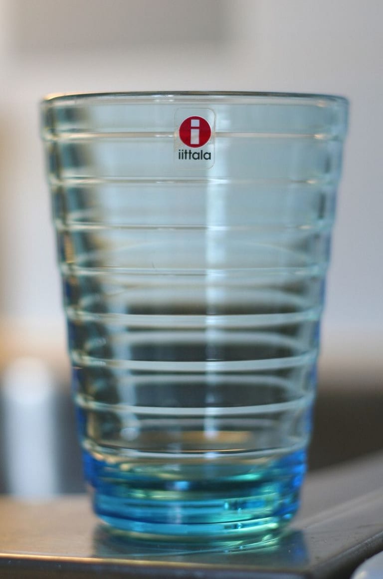 Ljusblått dricksglas med horisontella ringar runt hela glaset och Iittalas röda etikett