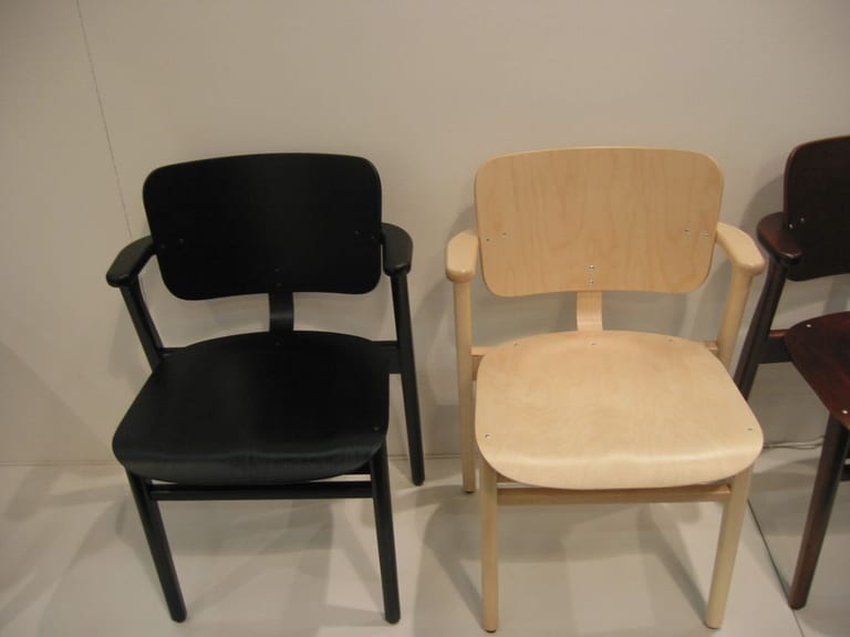 Två Domus-stolar av Ilmari Tapiovaara, en svart och en i ljust trä, med korta armstöd och sits och rygg i formpressad plywood