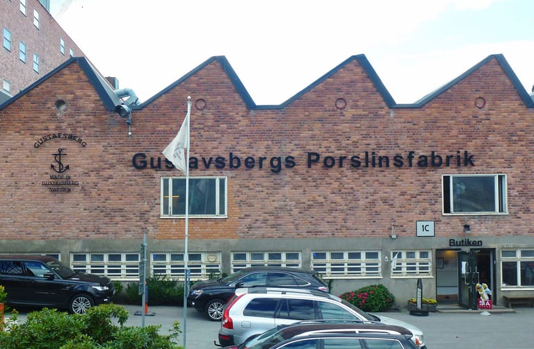 Tegelfasaden på Gustavsbergs porslinsfabrik med sågtandstak, skylten Gustavsbergs Porslinsfabrik och ingången till fabriksbutiken