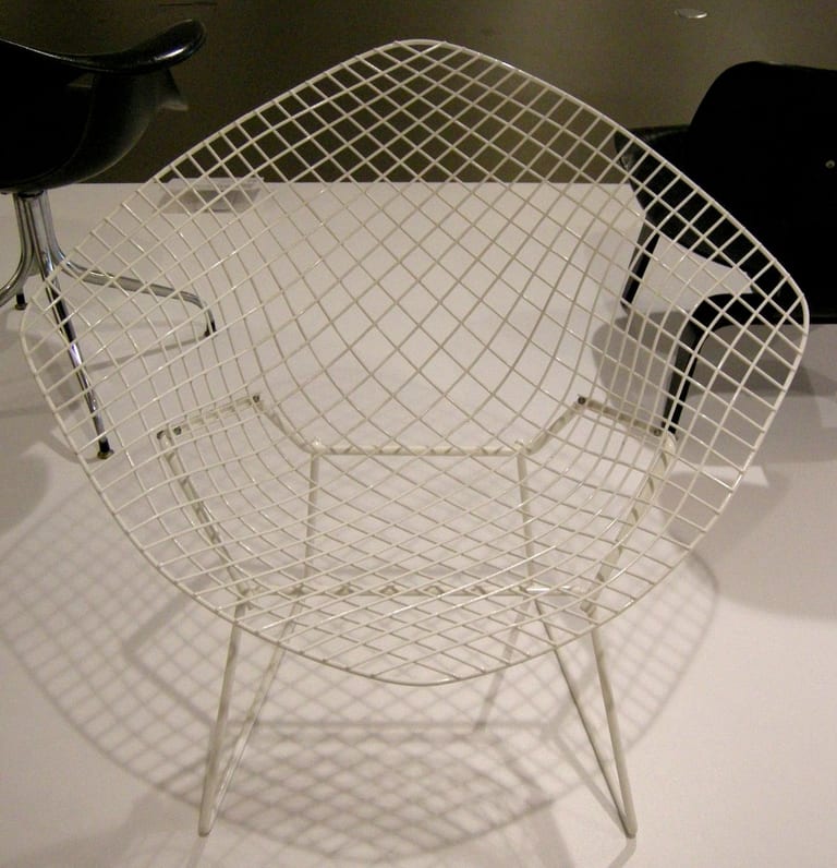 Vit Diamond Chair framifrån, ett nät av ståltråd som bildar sits, rygg och armstöd på ett underrede av stålstav