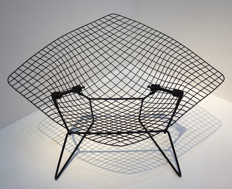 Svart Diamond Chair utan klädsel mot vit vägg, med trådnätets skugga på golvet