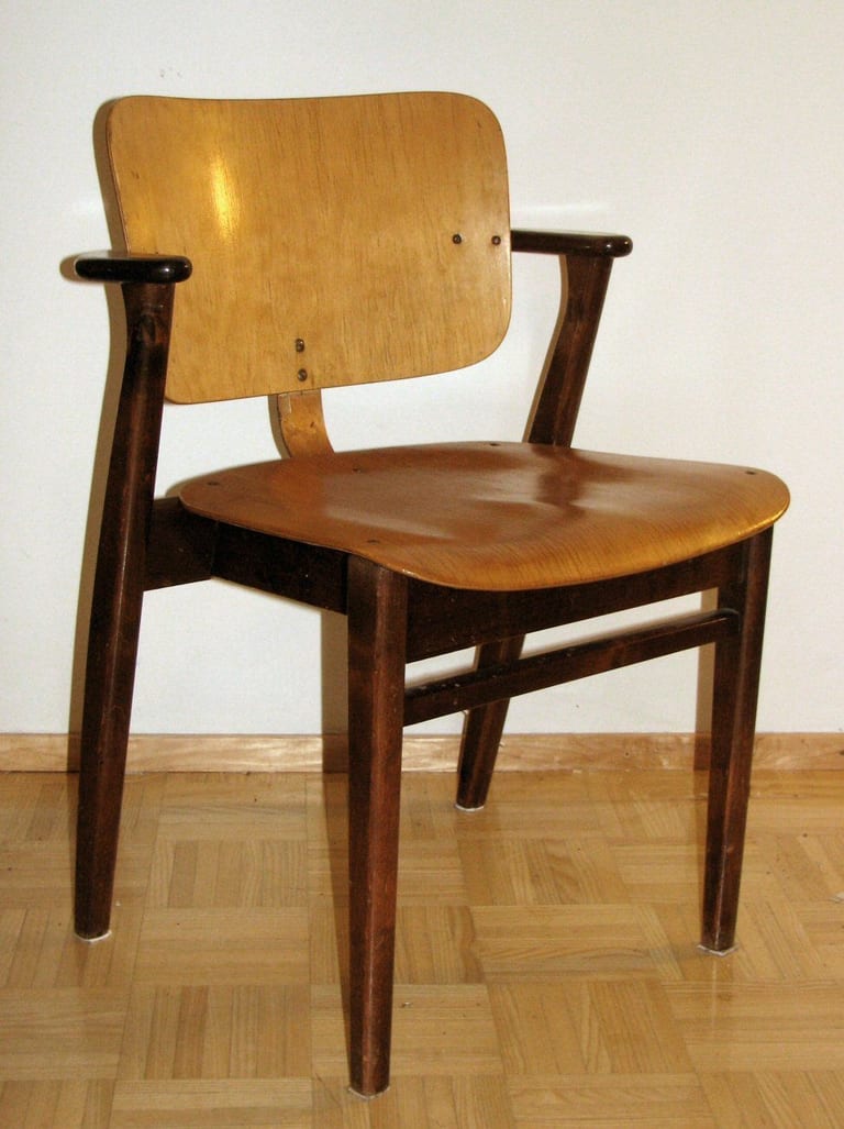 En äldre Domus-stol snett framifrån, med mörkbetsad ram och armstöd och sits och rygg i ljus, lackad plywood med synliga skruvar