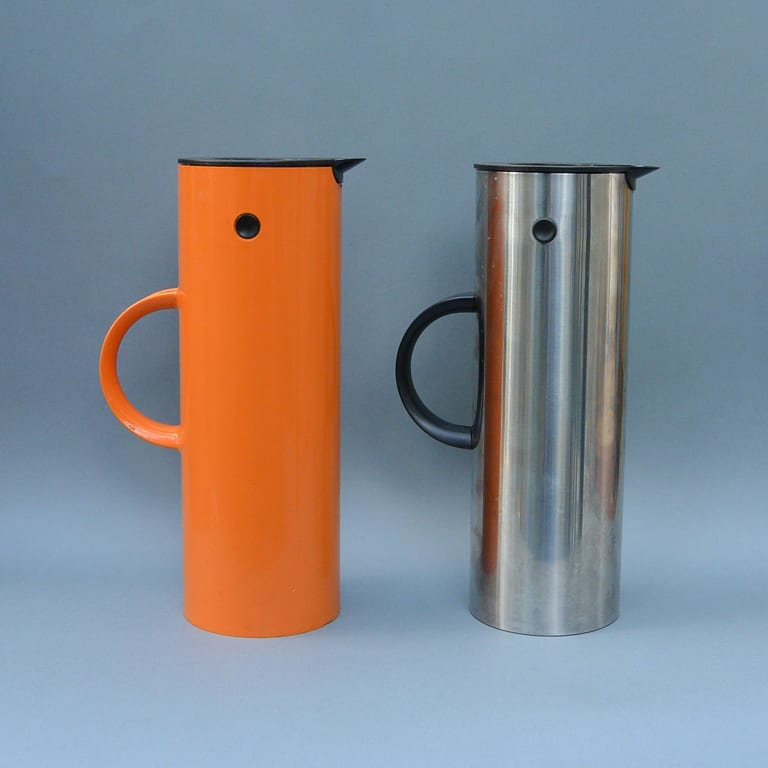 Två cylindriska termoskannor från Stelton, en i orange plast och en i rostfritt stål, med svarta lock