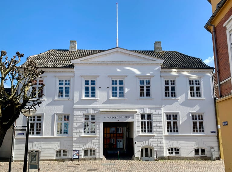 Faaborg Museums vita gatufasad med skylten Faaborg Museum över porten mot en kullerstensgata