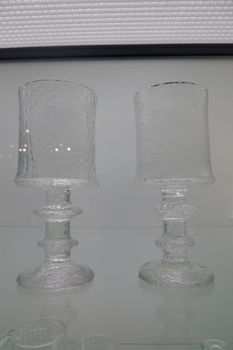 Två glas på fot med cylindrisk kupa i isliknande klarglas och ringad stam, i en monter