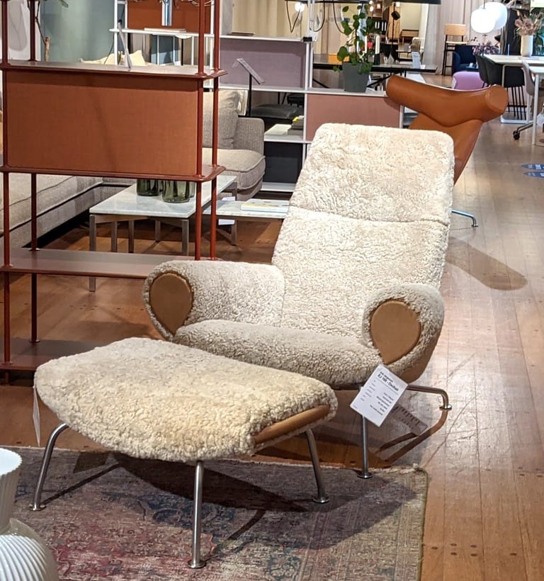 Hans J. Wegners Ox Chair utan horn, klädd i ljust lockigt fårskinn, med en matchande fotpall, och bakom den en Ox Chair i brunt läder med de hornliknande utskotten