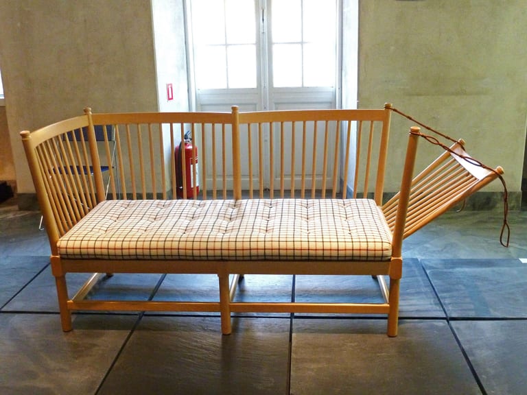 Børge Mogensens Tremmesofaen i ljust trä med spjälrygg och rutig sittdyna, med ena gaveln nedfälld och hållen av en läderrem, utställd på Designmuseum Danmark