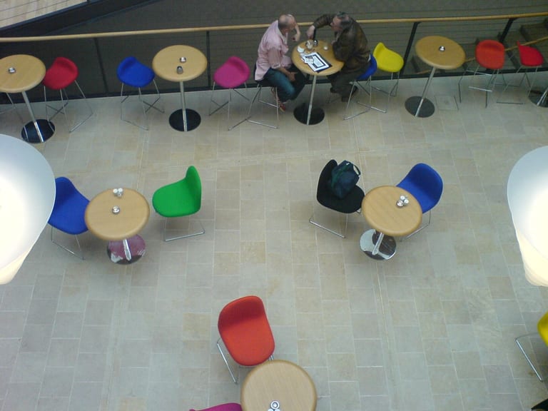 Röda, blå, gröna och svarta GUBI-stolar och barstolar runt runda bord i kaféet på Danish Design Centre, sett ovanifrån