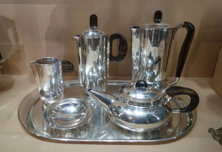 Te- och kaffeservis i blankt silver med handtag och knoppar i mörkt trä, på en oval silverbricka i en museimonter