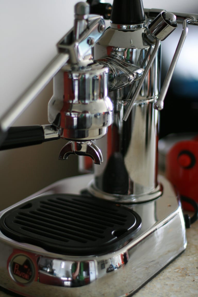 Närbild på en förkromad La Pavoni Europiccola: bryggruppen med filterhållare, ångröret och foten med logotyp och svart droppgaller