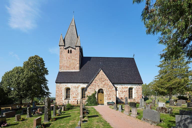 Finströms kyrka på Åland, en stenkyrka med spetsigt torn, sedd från kyrkogården