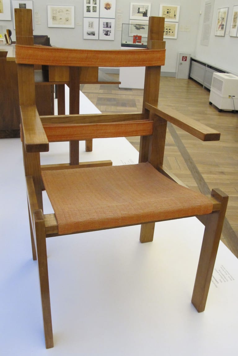 Marcel Breuers spjälstol Lattenstuhl ti 1a i ljust trä med orange dukar som sits och rygg, i en museisal
