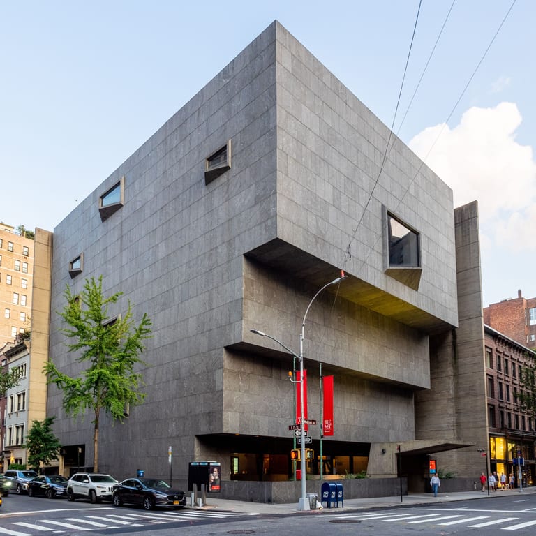 Breuer-byggnaden på Madison Avenue i New York, en mörkgrå stenklädd byggnad som kragar ut i steg över trottoaren, med banderoller för The Met Breuer