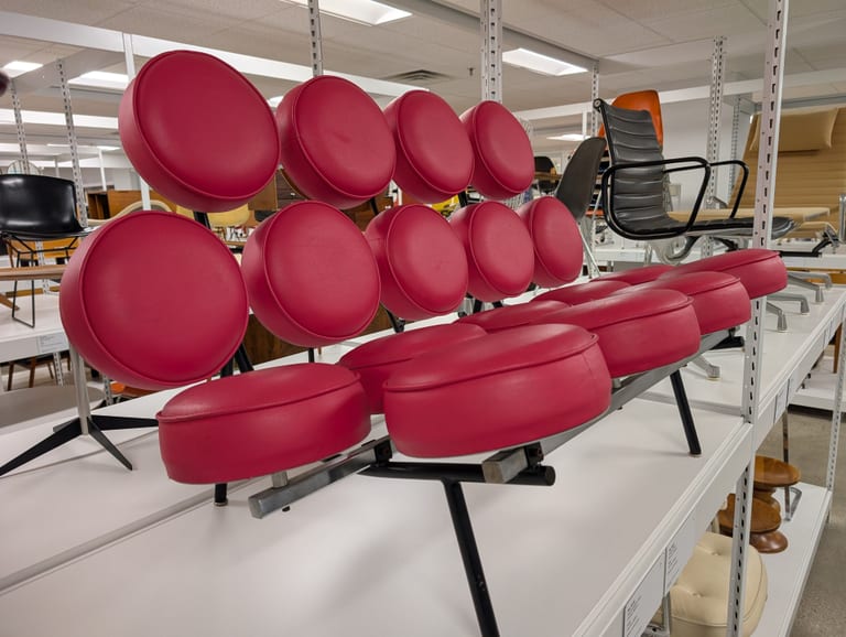 Röd Marshmallow Sofa snett framifrån bland arkivhyllor, med runda dynor som sitter var för sig på stålbalkar och svarta ben