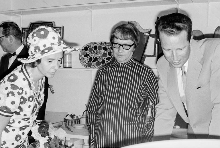 Svartvitt fotografi av Birger Kaipiainen i glasögon och randig skjorta, mellan drottning Fabiola i blommig hatt och klänning och kung Baudouin i ljus kostym