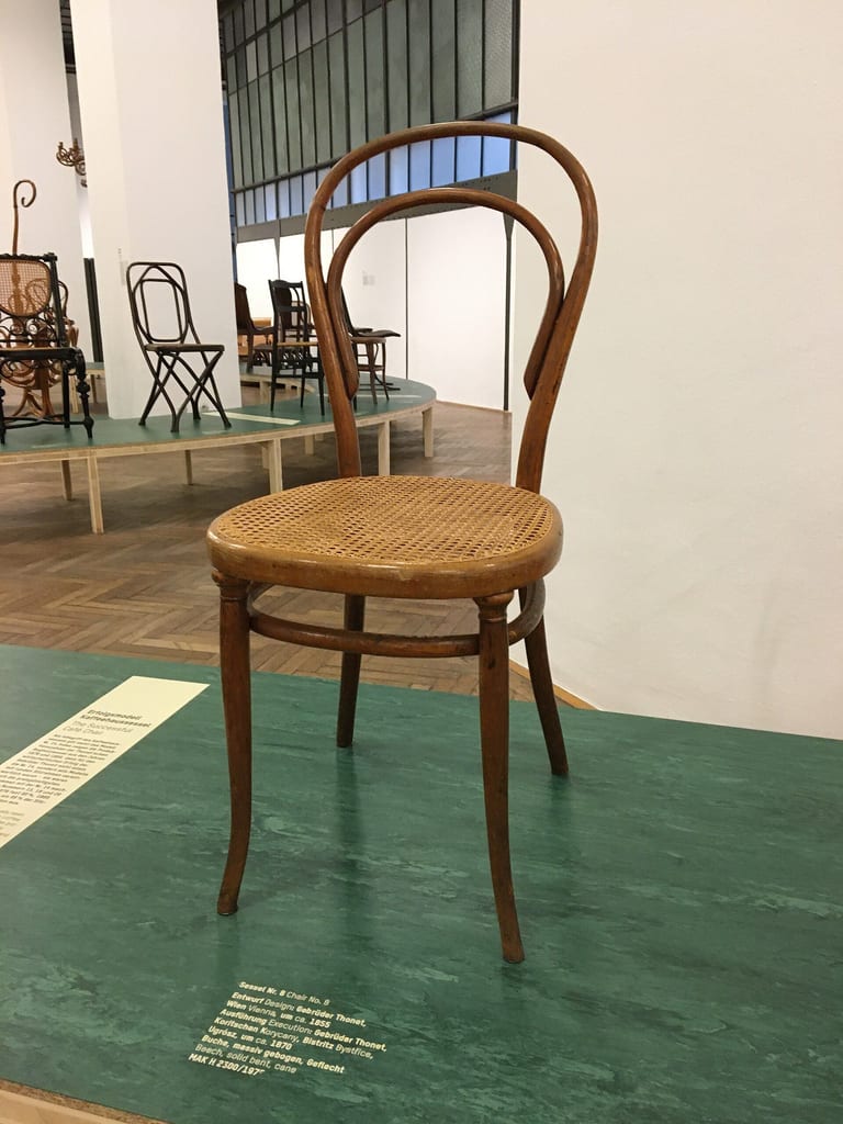 Böjträstol nr 8 från Gebrüder Thonet med rund rottingsits och ryggbåge med inre halvbåge, på ett grönt podium i en museiutställning