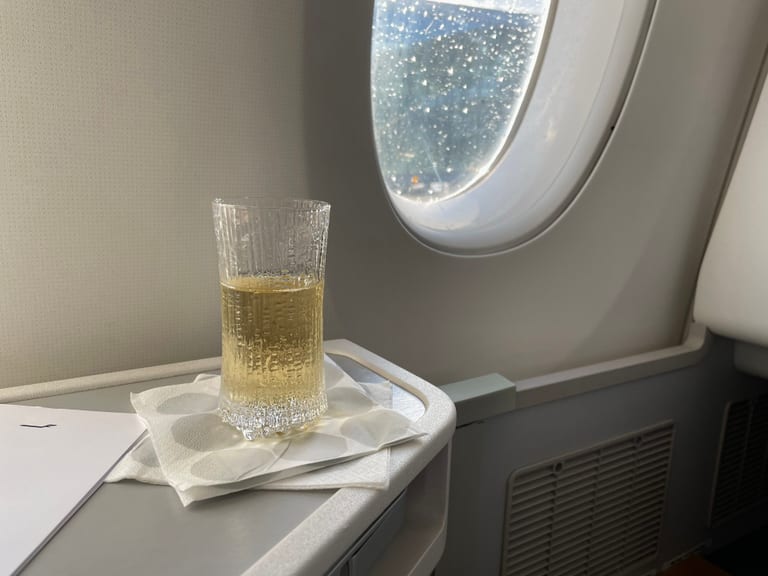 Ett högt Ultima Thule-glas med champagne på en servett vid fönstret i ett flygplan