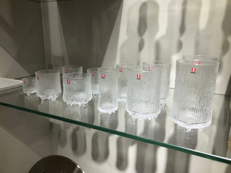 Ett tiotal Ultima Thule-glas i olika storlekar med Iittalas röda etiketter på en glashylla