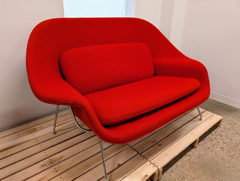 Womb Settee, Eero Saarinens tvåsits för Knoll, klädd i rött tyg med lösa dynor på förkromat stålstångsunderrede